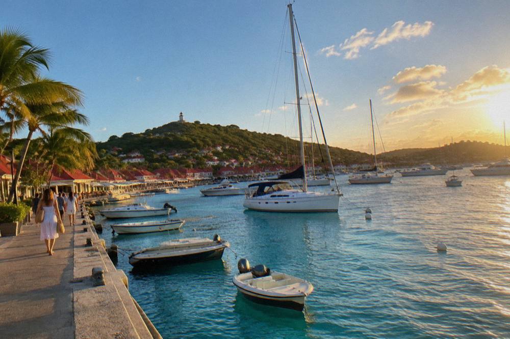 Yachts anchored in a small Caribbean harbour town with red roofs at golden hour