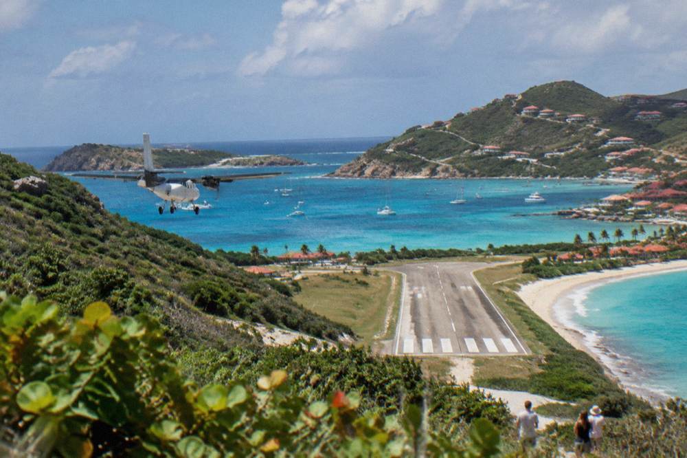 A small turboprop airplane on a short runway between a hillside and a Caribbean bay