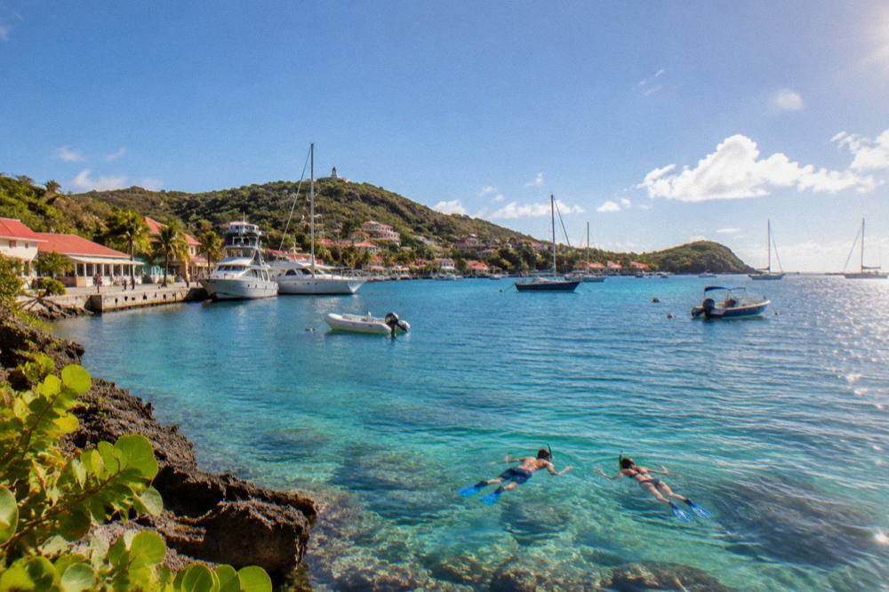Snorkellers in clear shallow water over coral near a rocky Caribbean point