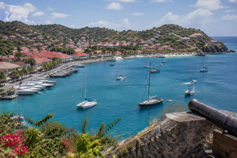 Sunlit harbor of Gustavia seen from a hillside fort with sailboats and clear blue water below