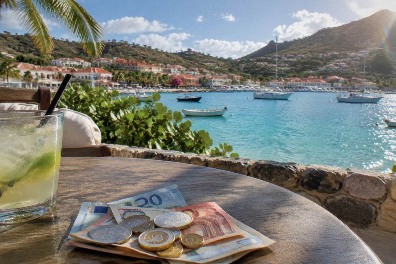 Euro banknotes and coins resting on a cafe table beside a view of turquoise Caribbean water
