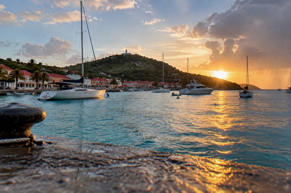 A sunset over Gustavia harbour with yachts at anchor and red roofs along the shoreline