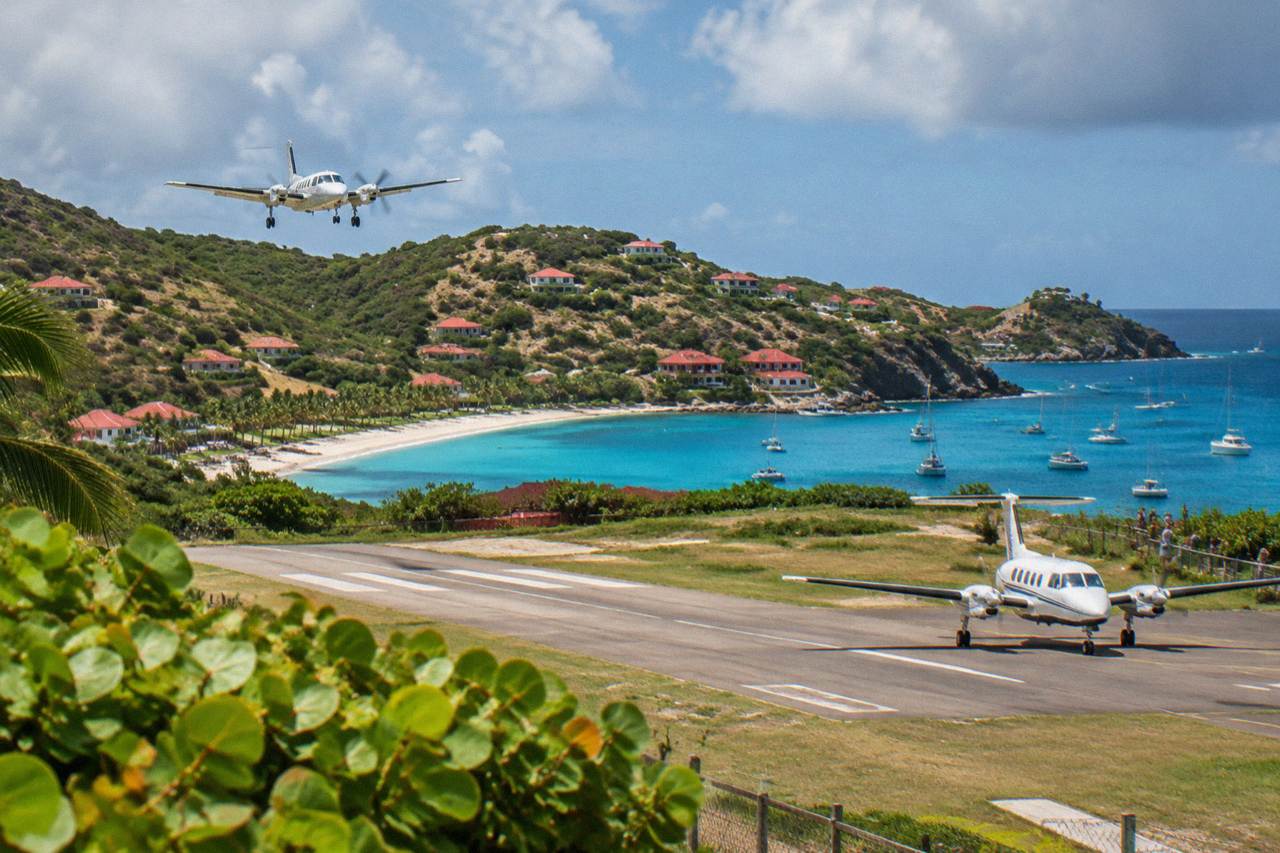A small turboprop aircraft parked on a short runway between green hills and a Caribbean bay