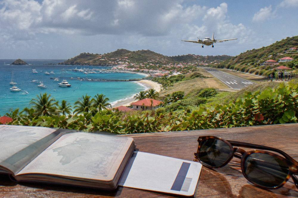 A passport open on a wooden counter beside a boarding pass and sunglasses