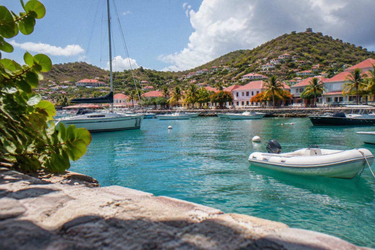 Sunlit harbor town with red roofs and boats moored in clear turquoise water