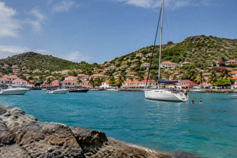 White sailboat anchored near a rocky green island with people preparing to swim