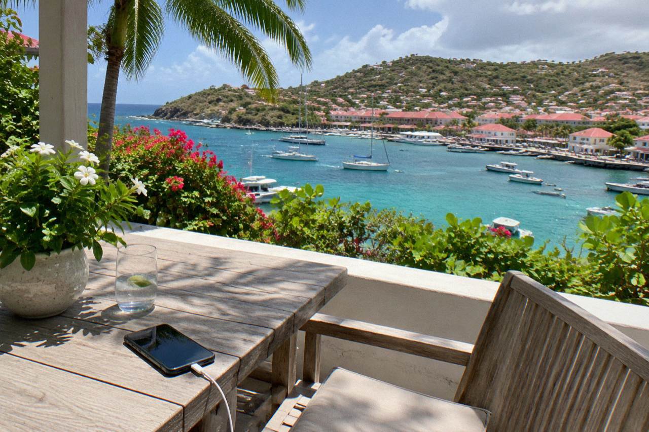 A villa terrace in St Barts with a phone charging on a table beside a view of turquoise water