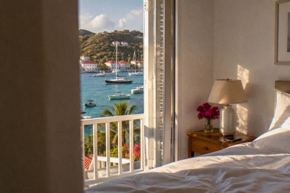 A whitewashed villa bedroom in St Barts with a bedside table, lamp and a phone on a charger