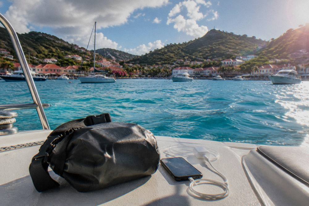 A dry bag with a phone and charger sitting on the deck of a boat in clear Caribbean water
