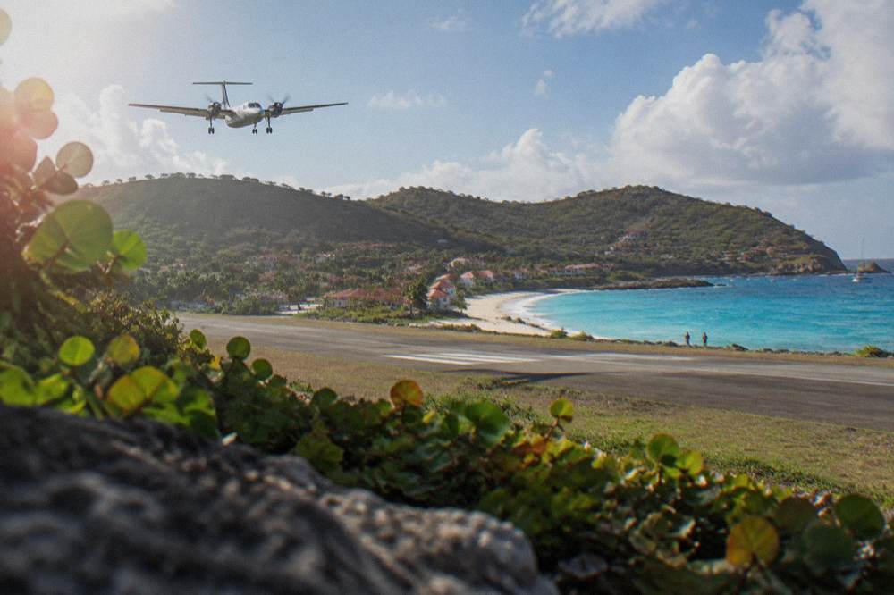 A small turboprop aircraft on a short runway beside a beach with hills behind it