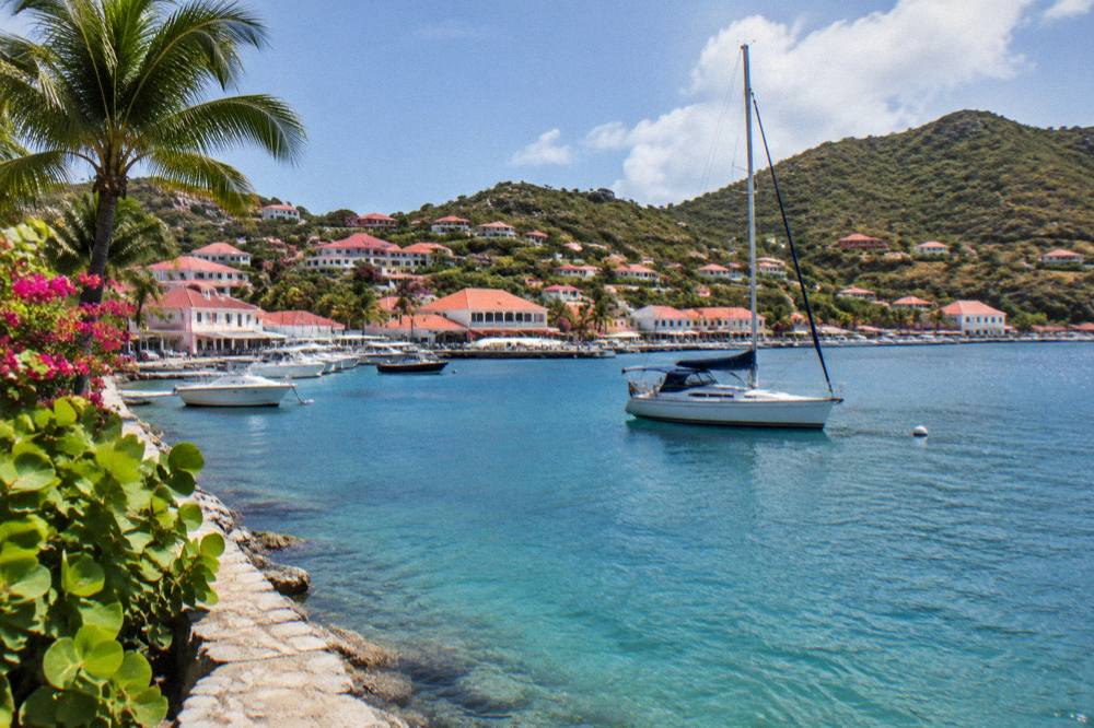 A sailboat anchored in a calm bay with green hills rising behind it