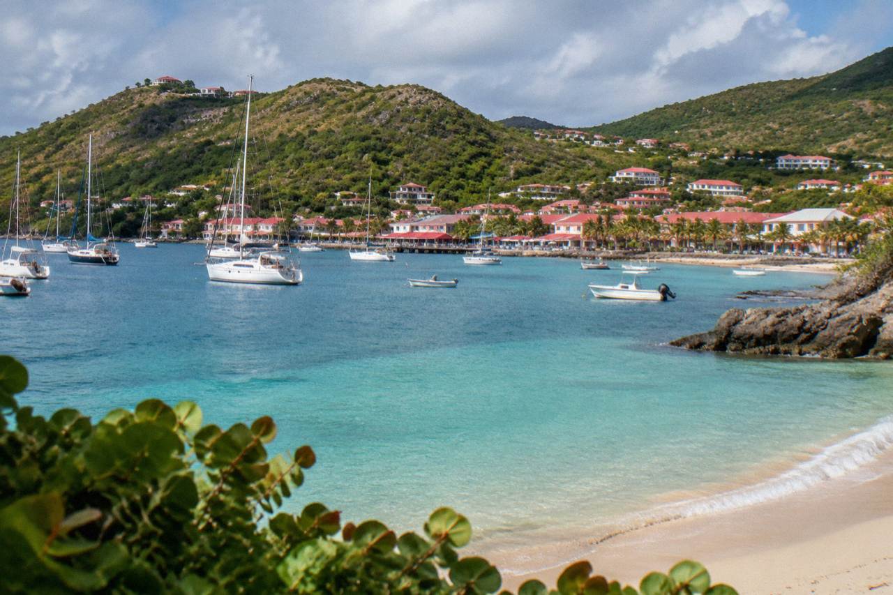A calm crescent beach on St Barts with shallow turquoise water and green hills behind