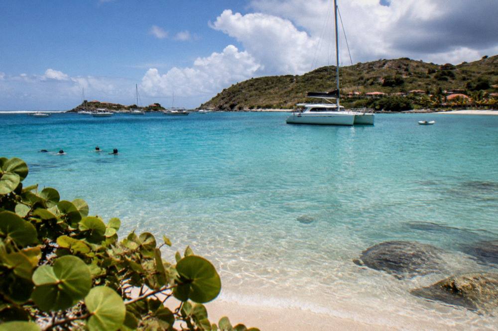 A catamaran moored in a quiet bay with people snorkeling near the shore