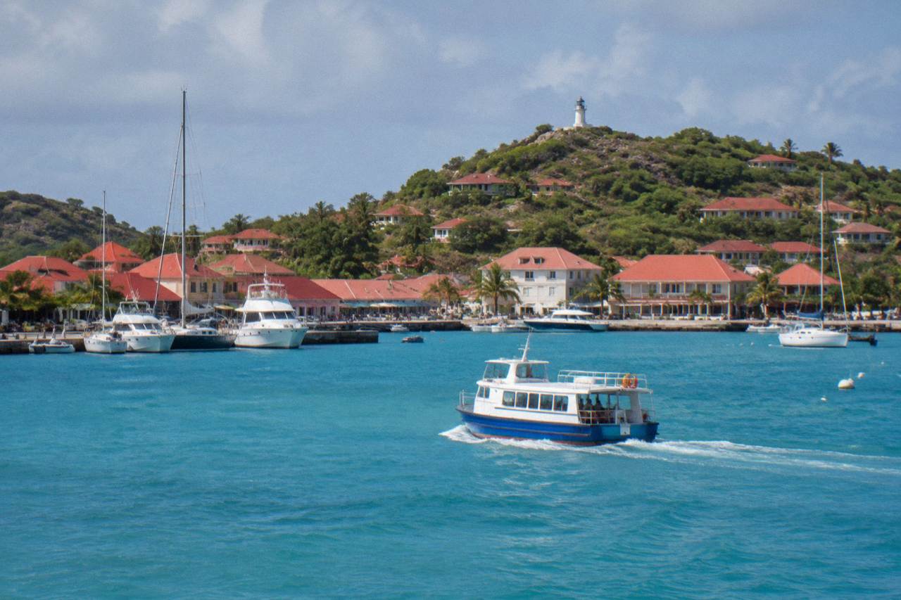 A small ferry boat crossing turquoise Caribbean water toward a green island coastline