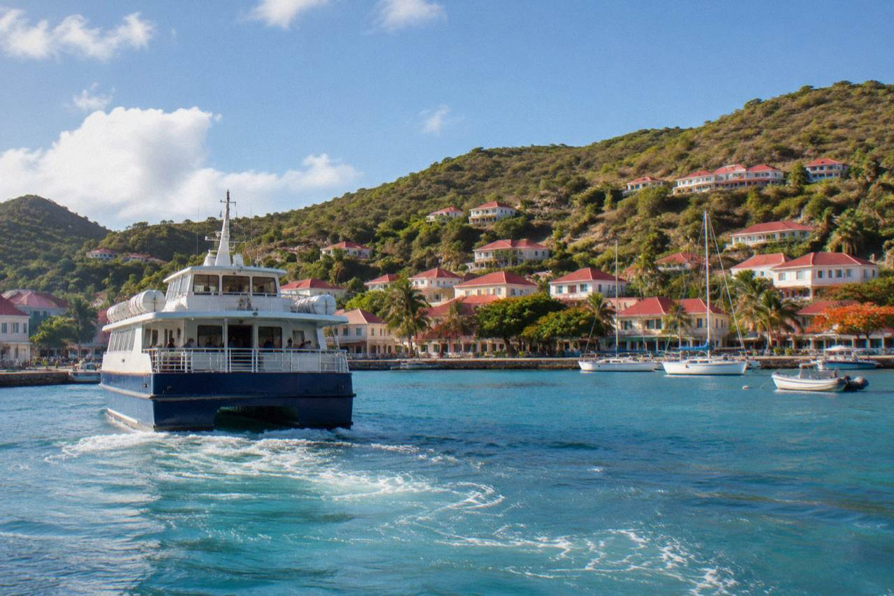 A passenger ferry arriving at the small harbour in Gustavia, St Barts, with hills and red roofs behind it