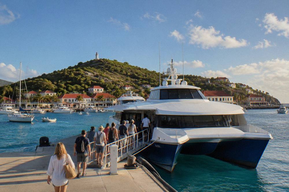 A fast catamaran ferry moored at a Caribbean marina with passengers boarding in bright morning light