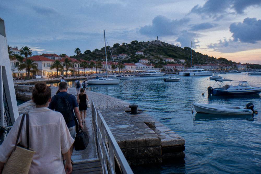 Passengers with bags walking down a ferry gangway onto a stone quay in a Caribbean harbour town