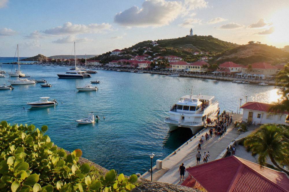 A small marina in the Caribbean with a white ferry at the dock and passengers waiting with bags