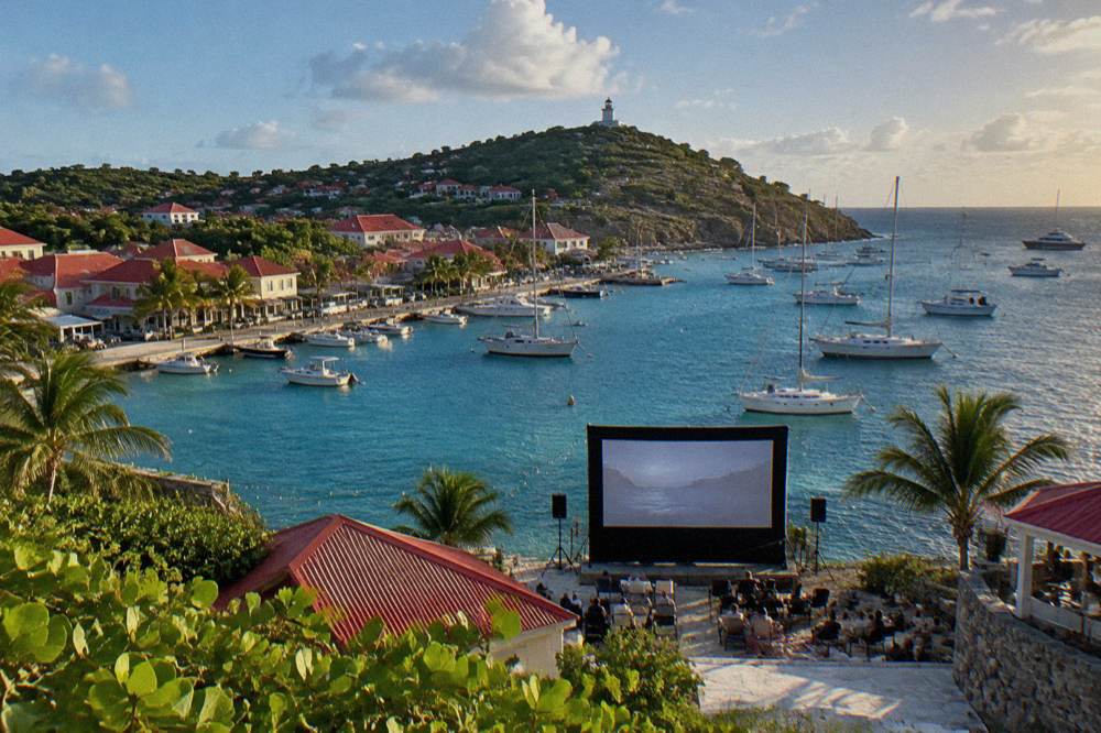 An outdoor film screen set up as dusk falls near the shore