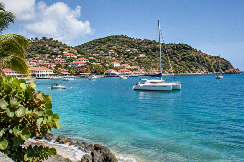 A catamaran anchored in a calm turquoise bay with a wooded headland behind it