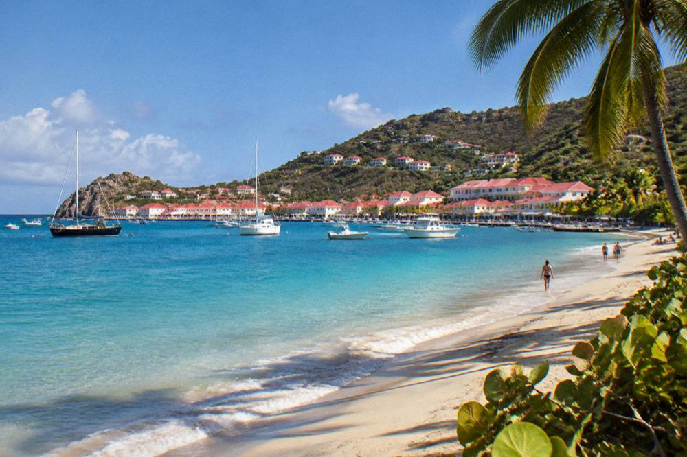 A sandy Caribbean beach with gentle waves and a few people under palm trees at golden hour