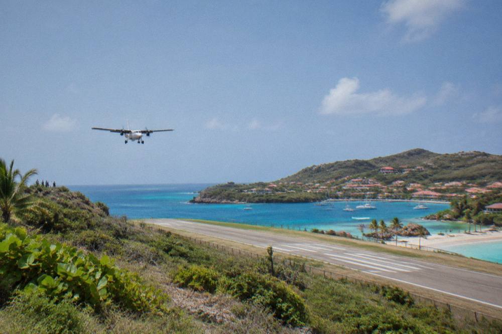 A small turboprop aircraft parked on a short runway between green hills and the sea