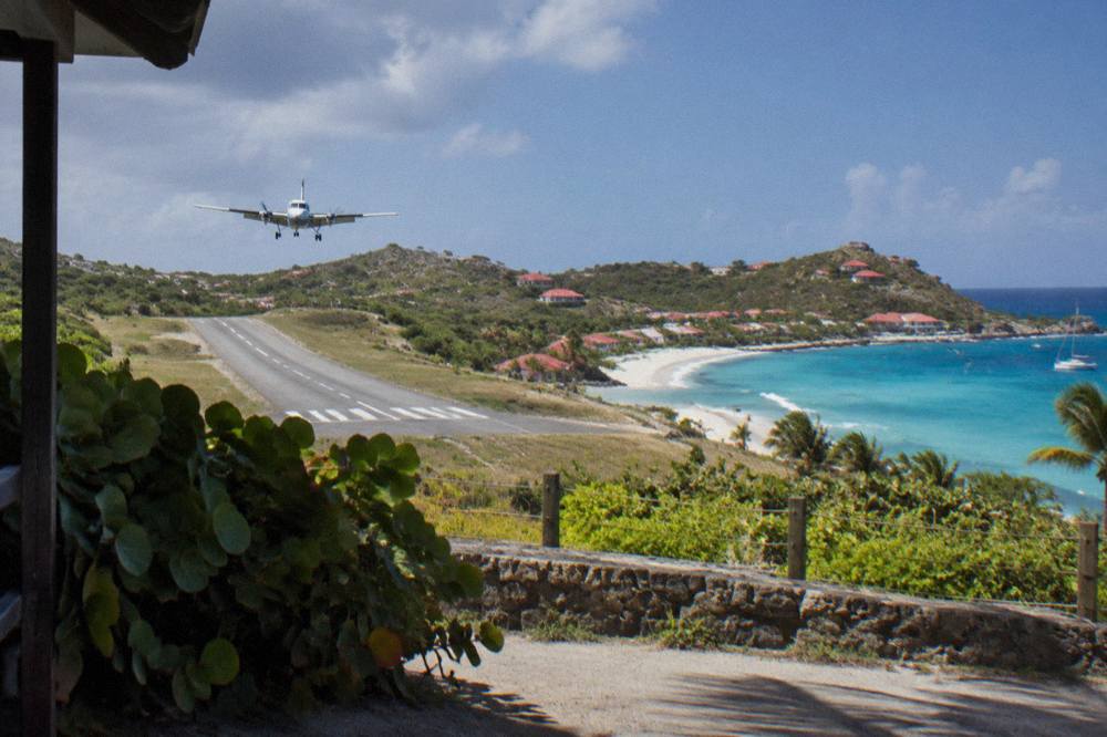 A small turboprop aircraft on a short runway between a beach and hills