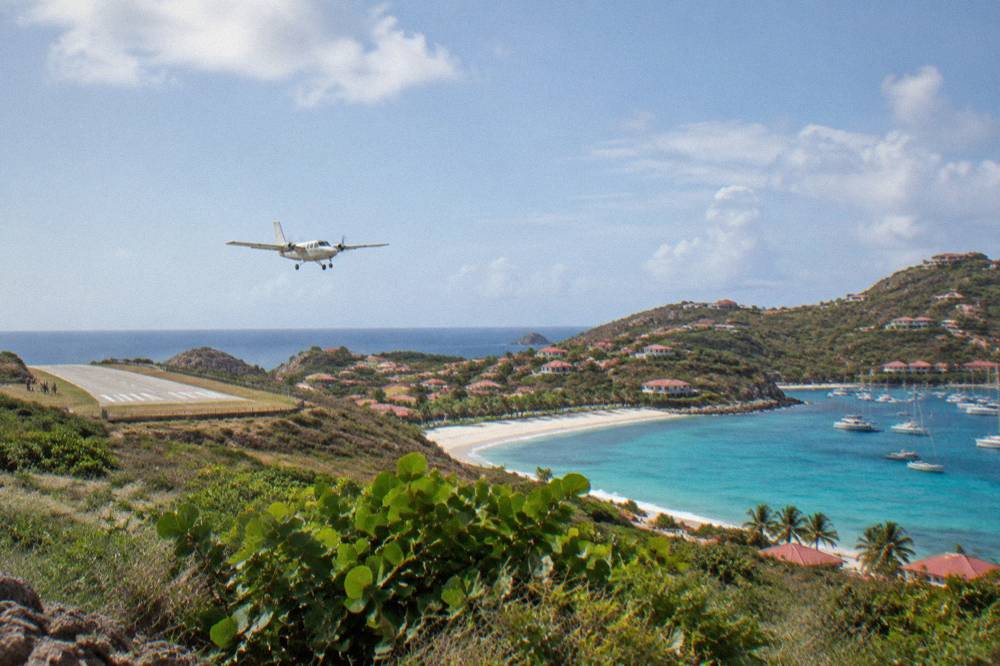 A light aircraft descending toward a coastal runway with calm sea on either side