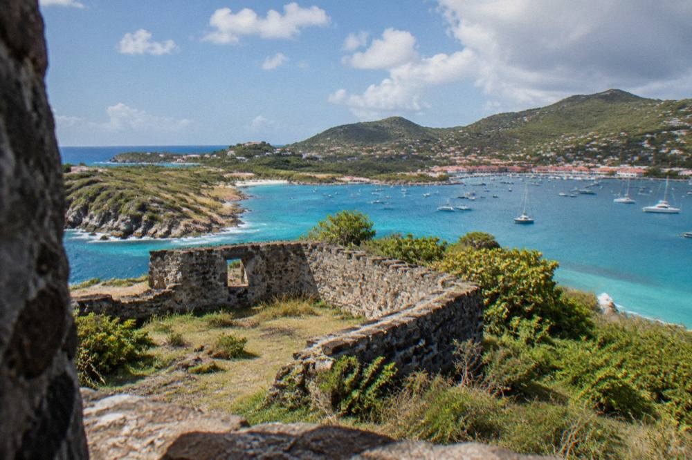 Stone fort ruins on a green headland overlooking a harbor with sailboats