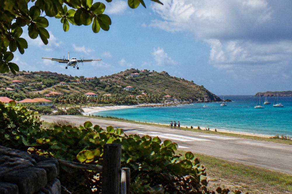 A small turboprop aircraft on a short runway beside a beach and turquoise bay