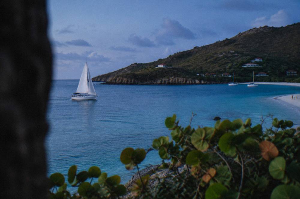 A sailboat cutting across open blue water toward green hills