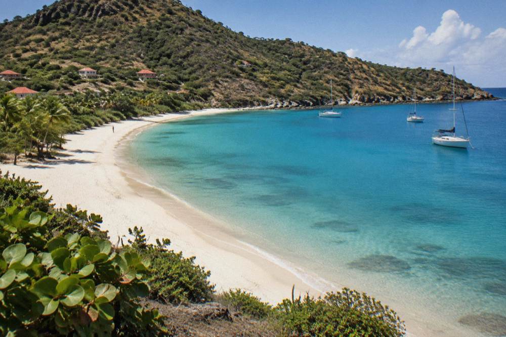 A wide empty bay of pale sand and clear water between green headlands
