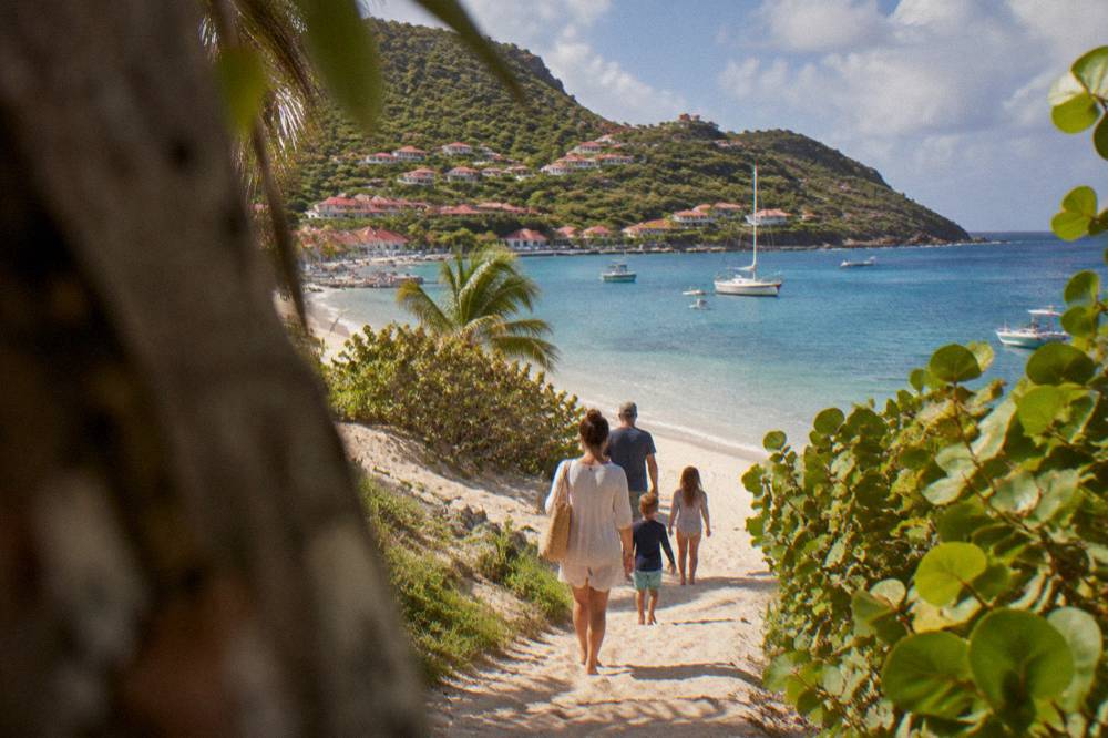 A family walking a sandy path toward a calm Caribbean beach