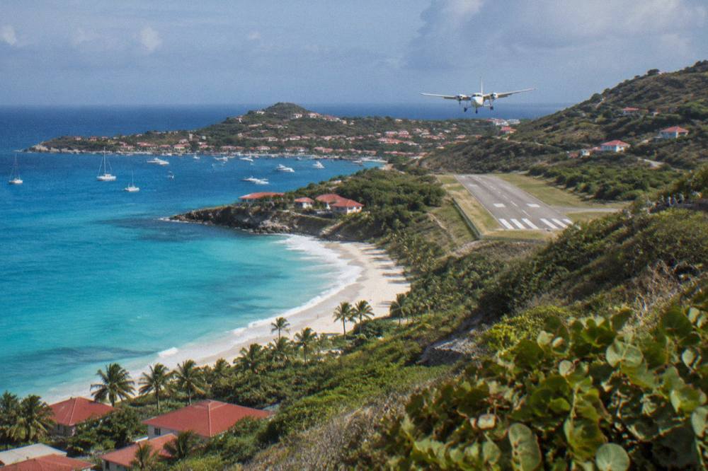 A small plane on a short runway between a beach and green hills