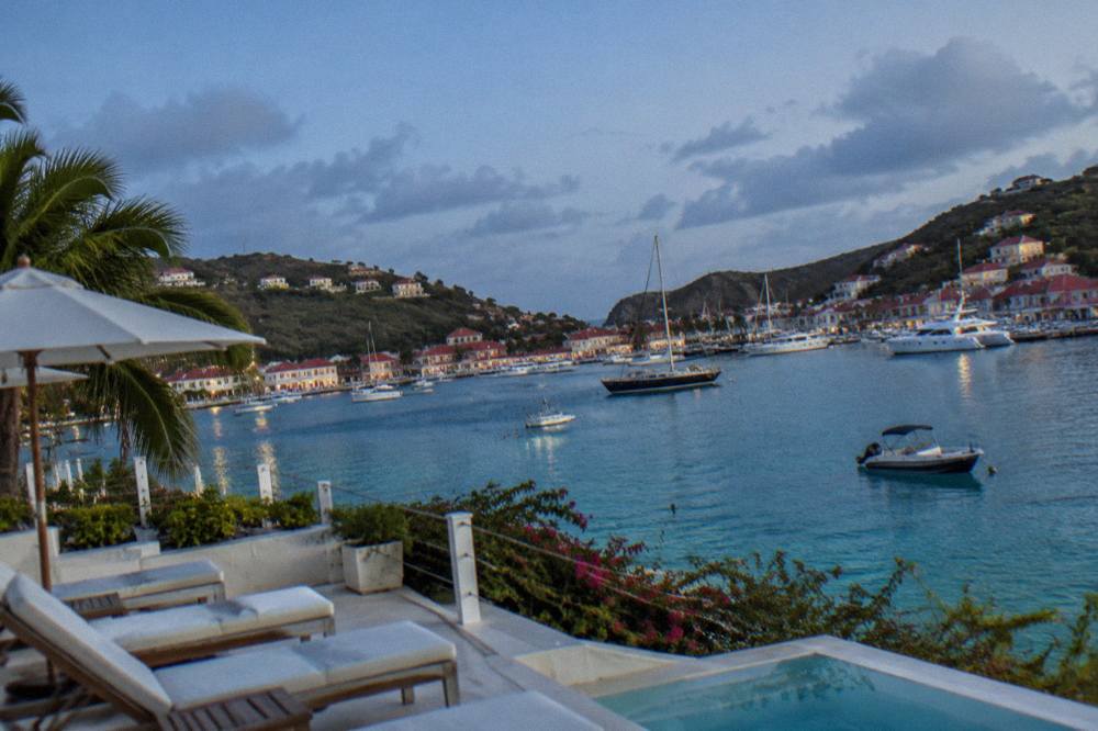 A white hotel terrace overlooking a calm turquoise bay with sun loungers
