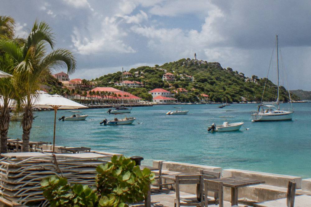 Shuttered beach chairs stacked beside an empty terrace overlooking a calm Caribbean bay