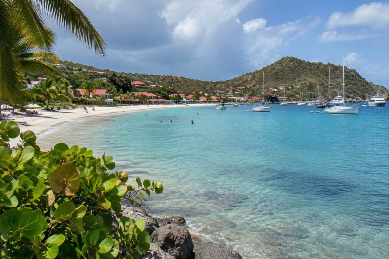 Sailboats anchored in turquoise water below green hills on a Caribbean island