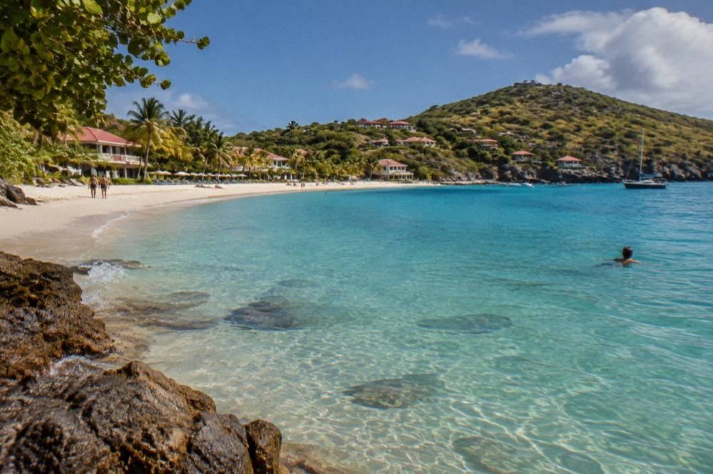 Clear shallow water over sand with a person swimming near a rocky point