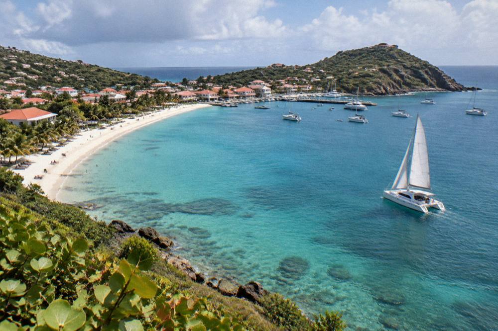 A catamaran under sail approaching a rocky green island in open water