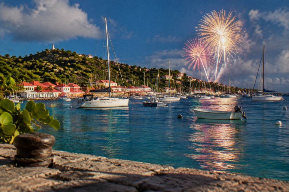 Fireworks bursting above a harbor full of boat masts at night