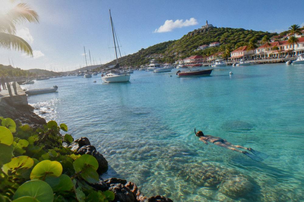 A snorkeler swimming over coral in clear shallow water