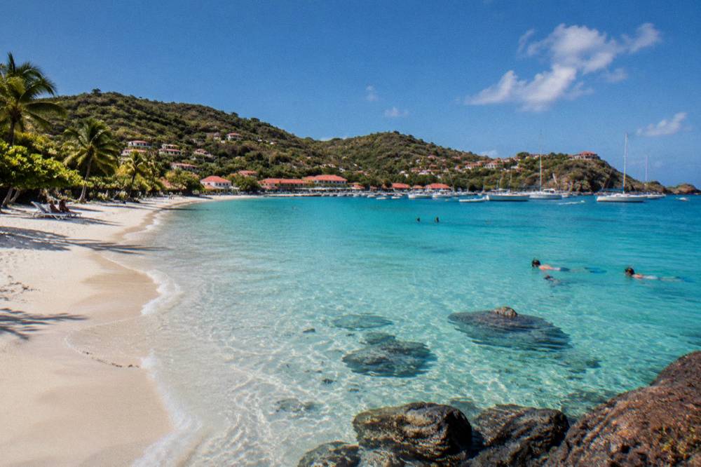 Snorkellers in clear shallow water above rocks and small fish near a beach