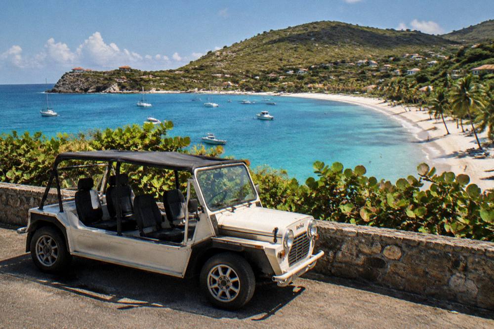 An open-air Mini Moke parked beside a low stone wall with sea view beyond