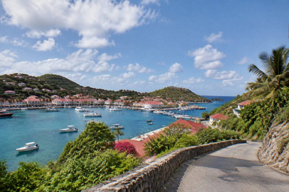 A narrow winding road climbing a green hill with sea views in St Barts