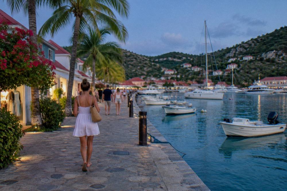 People walking a stone quay past boutiques under palm trees in Gustavia