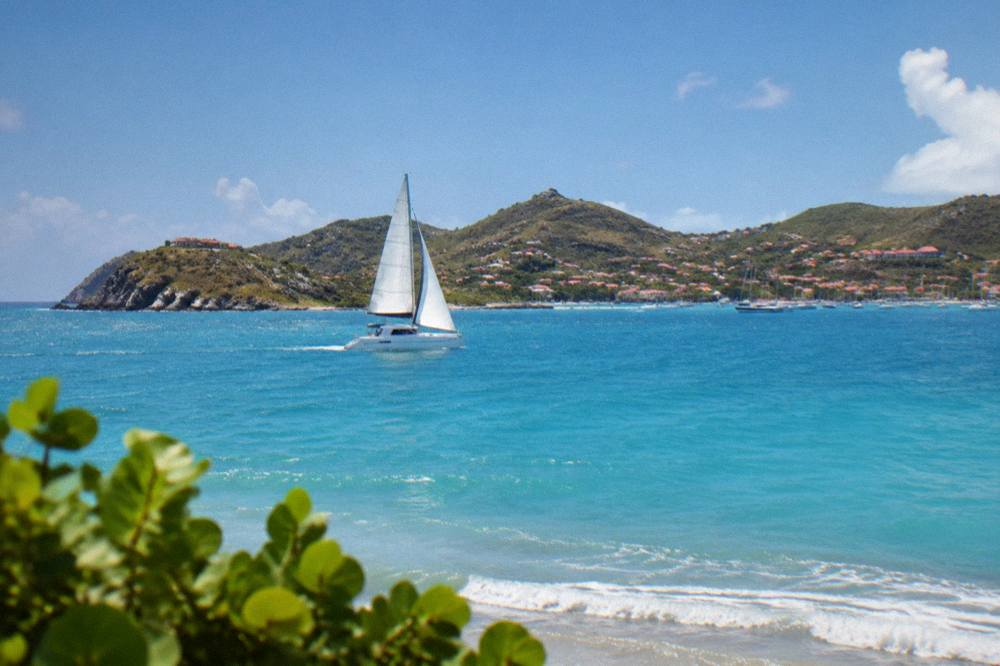 A catamaran under sail on open blue water toward the hills of St Barts