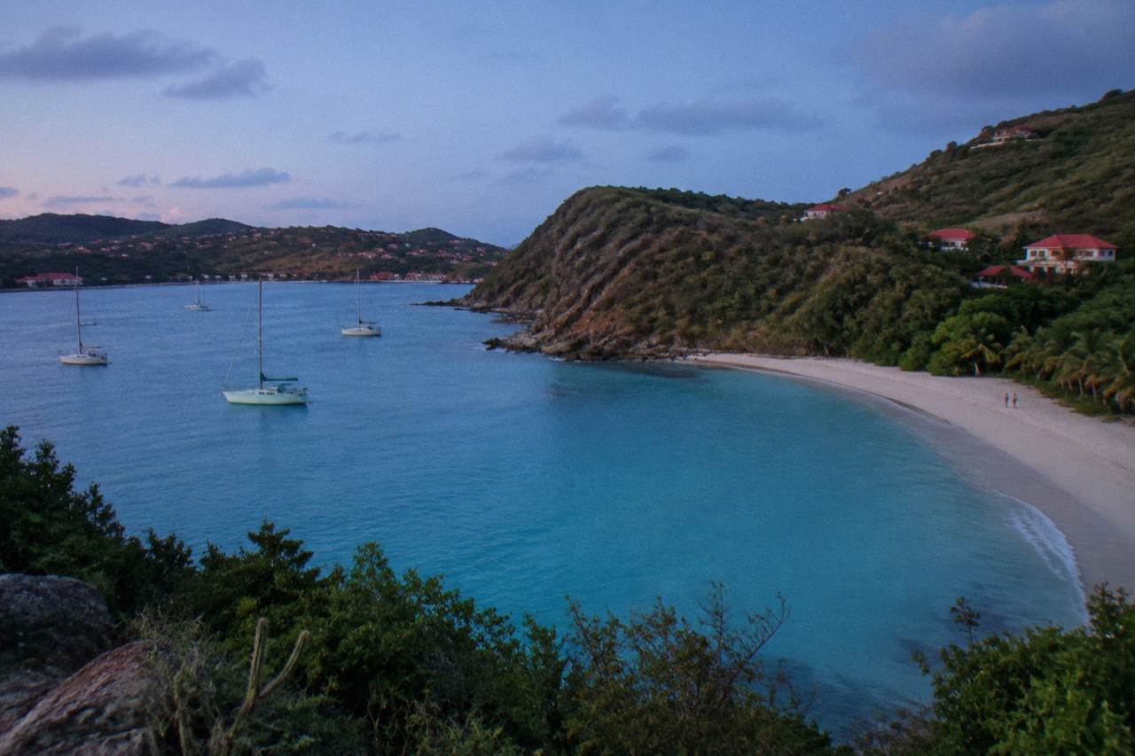 A view across turquoise water toward green hills with red roofs on a Caribbean island coastline