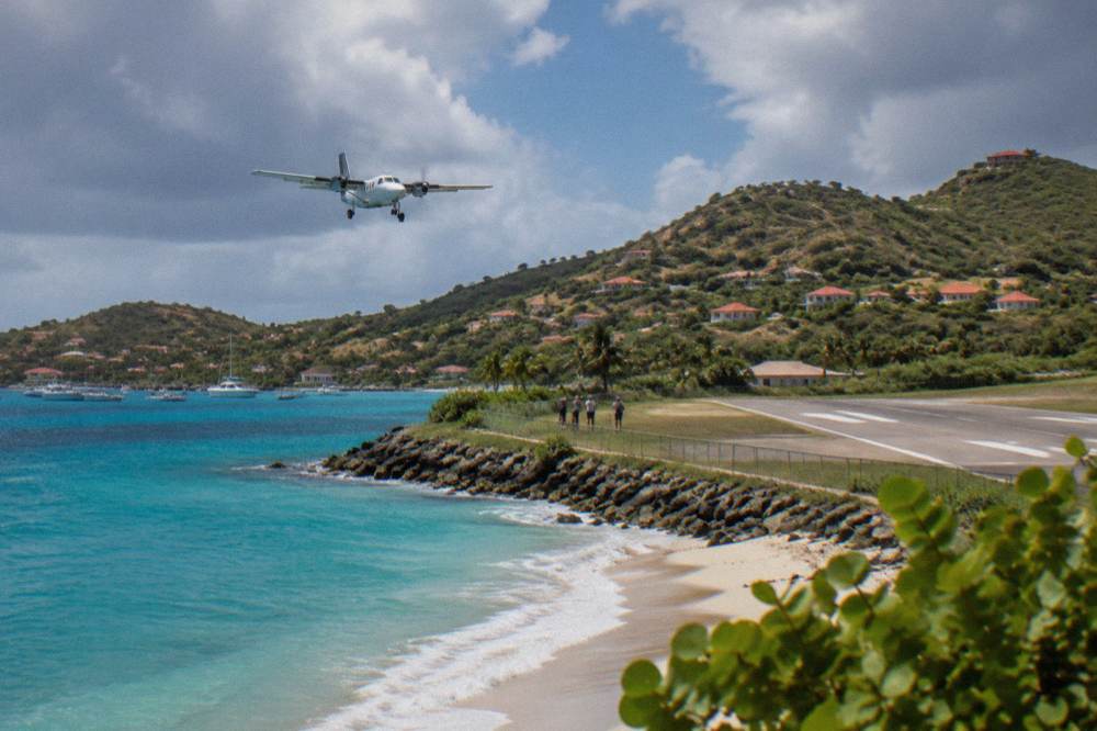 A small turboprop aircraft on a short runway beside a beach and green hills