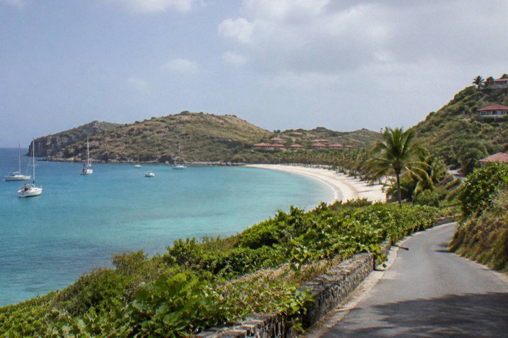 A narrow road winding up a green hillside above the sea on a small Caribbean island