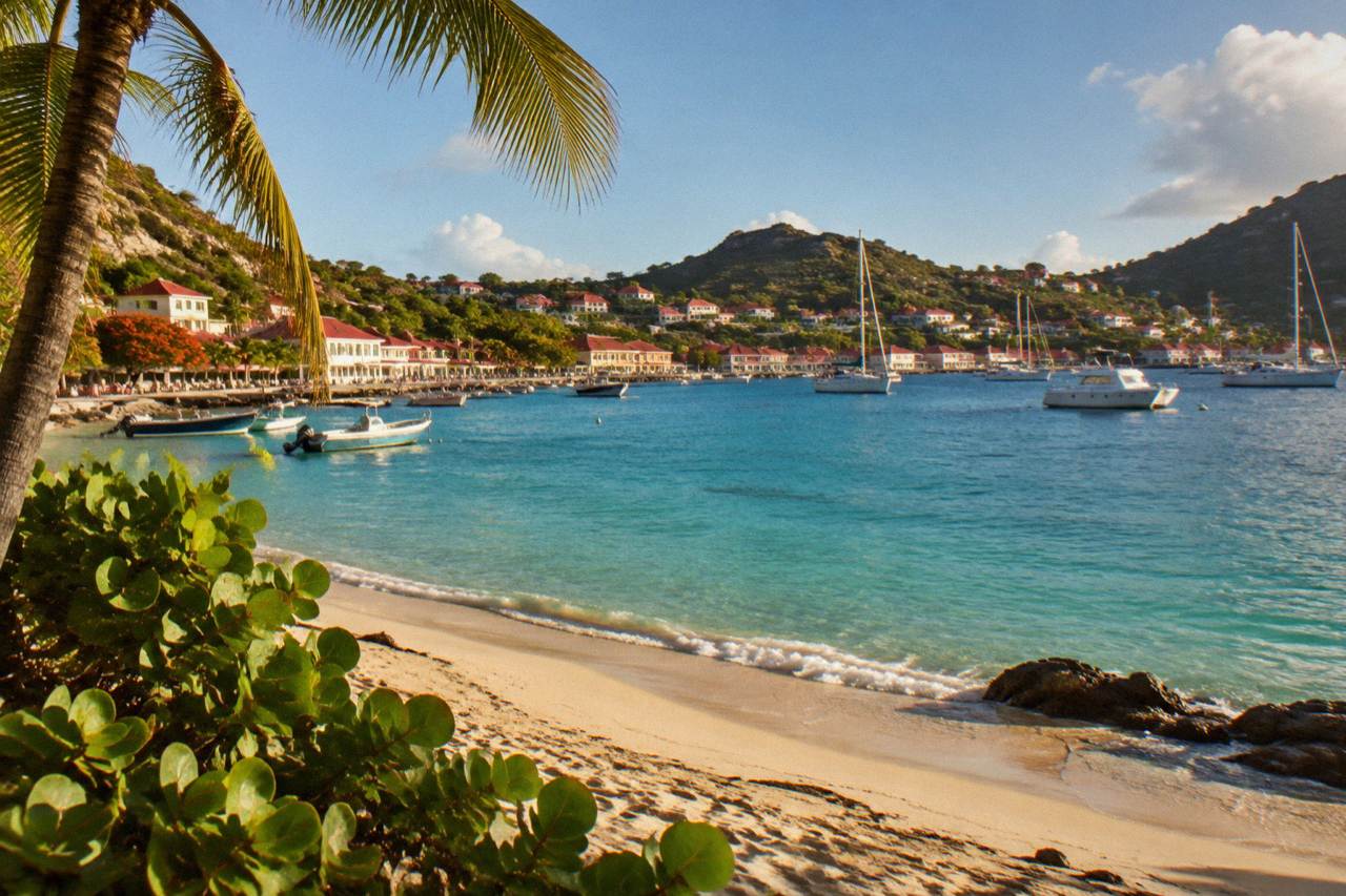 A calm Caribbean beach on St Barts with clear turquoise water and green hills under a sunny sky